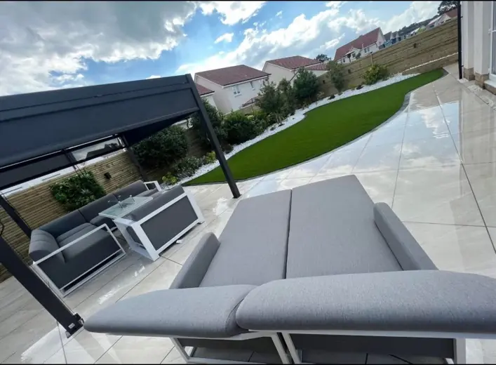 Light porcelain patio with black pergola and artificial grass installed by Indie Paving